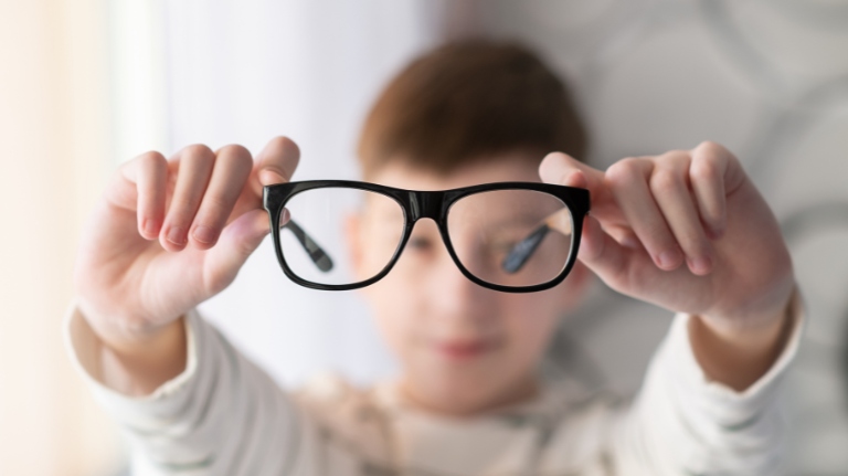Child holding eyeglasses to show the difference between blurry and clear vision from myopia