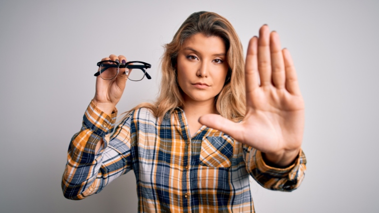 Adult demonstrating blurry vision caused by myopia by holding glasses in front of her face